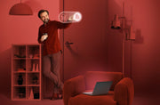 Man in a red room with a laptop on a chair and a shelf.