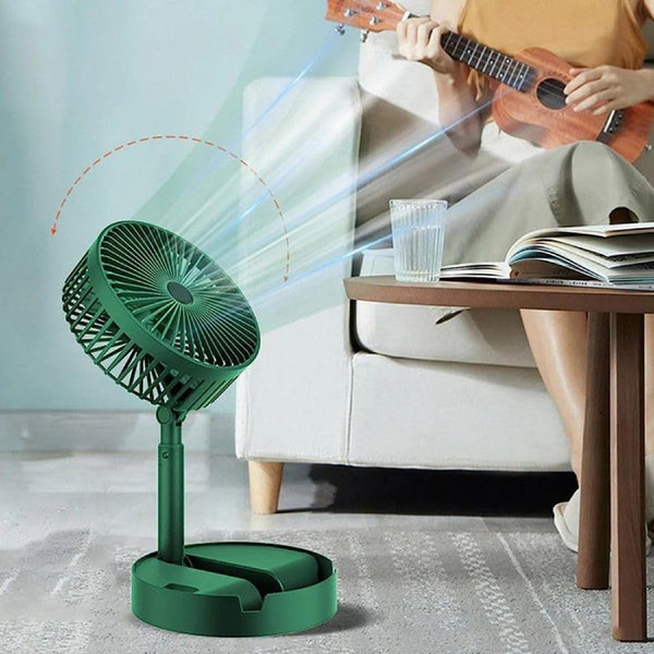 Green fan blowing air towards a person sitting on a couch with a glass of water and a book.